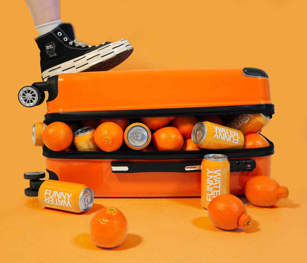 Orange suitcase with fruit and cans of Funny Water