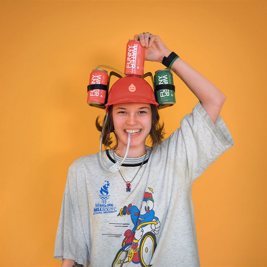Woman with a hat contraption holding three cans of Funny Water