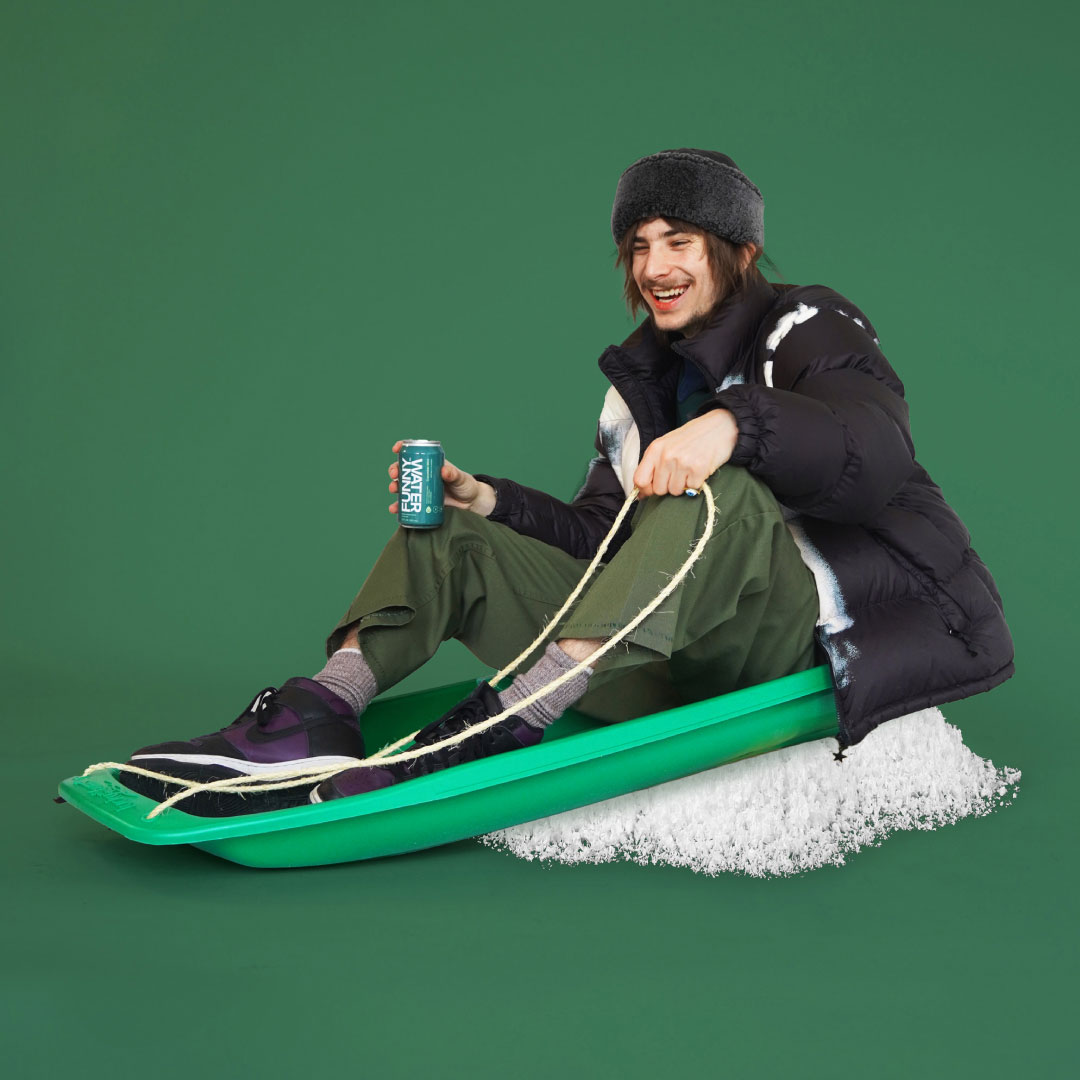 Man on a snow sled holding a can of Funny Water